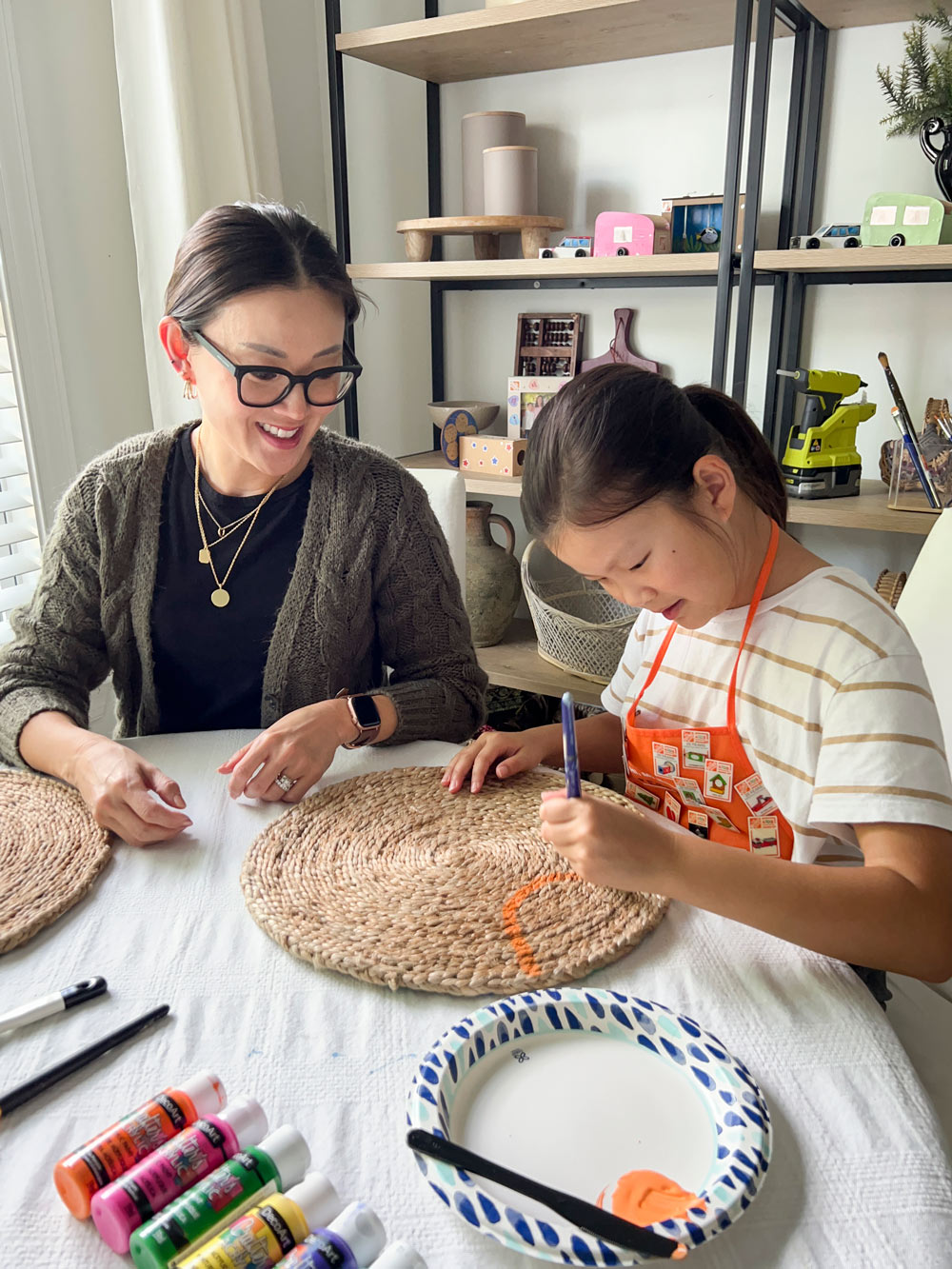 Two people painting a placemat with orange paint.