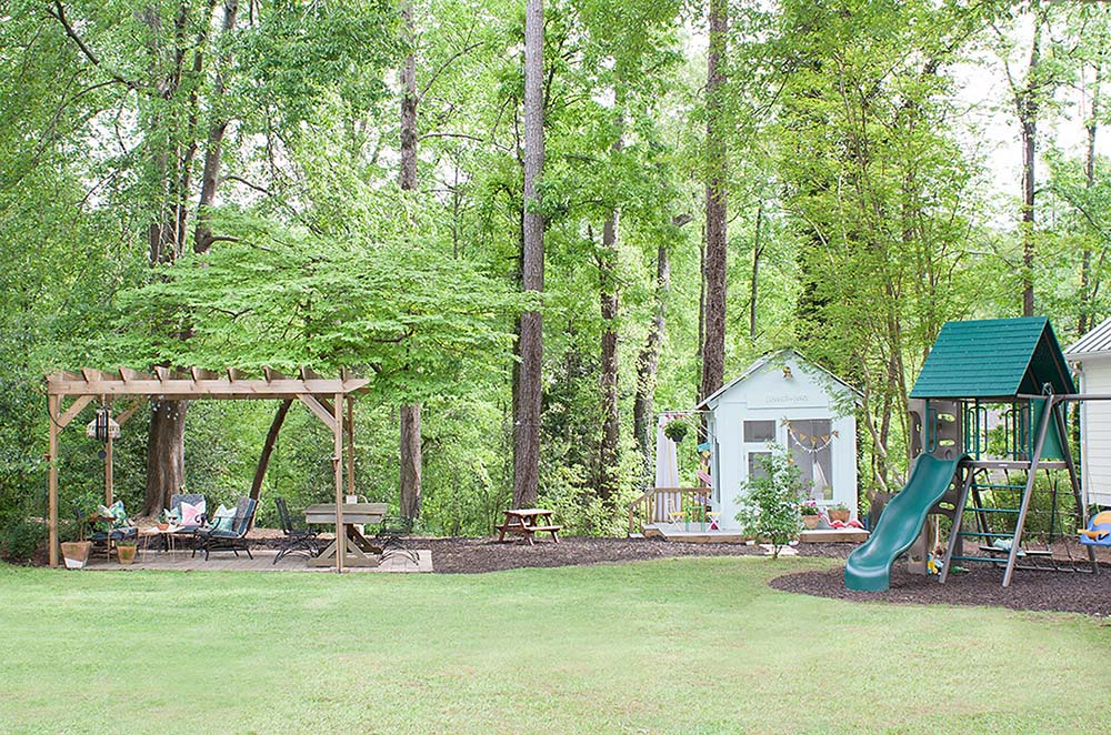 A large backyard with a pergola, swing set, and kid's playhouse.