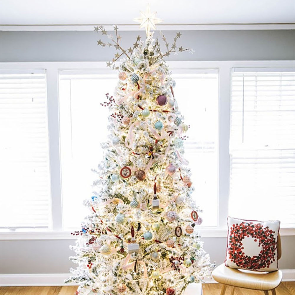A decorated Christmas tree sits on hardwood floors in front of a wall of windows.