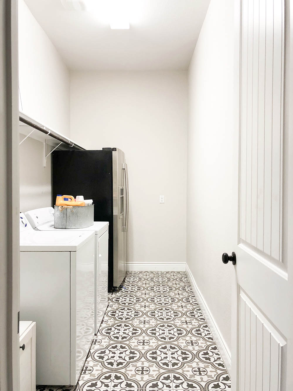 Laundry room with a white door, mosaic tiled flooring, white washer and dryer, and a refrigerator. 