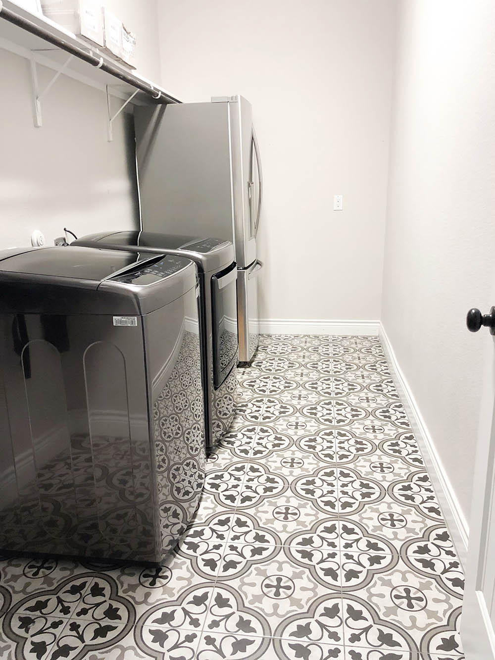 Laundry room with mosaic tiled flooring, black washer and dryer, and a refrigerator. 