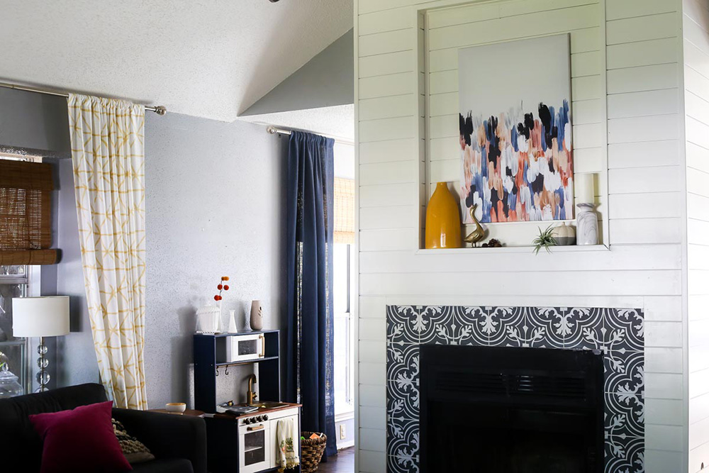 A living room with furniture and a fireplace with mosaic tile, shiplap and wall art.