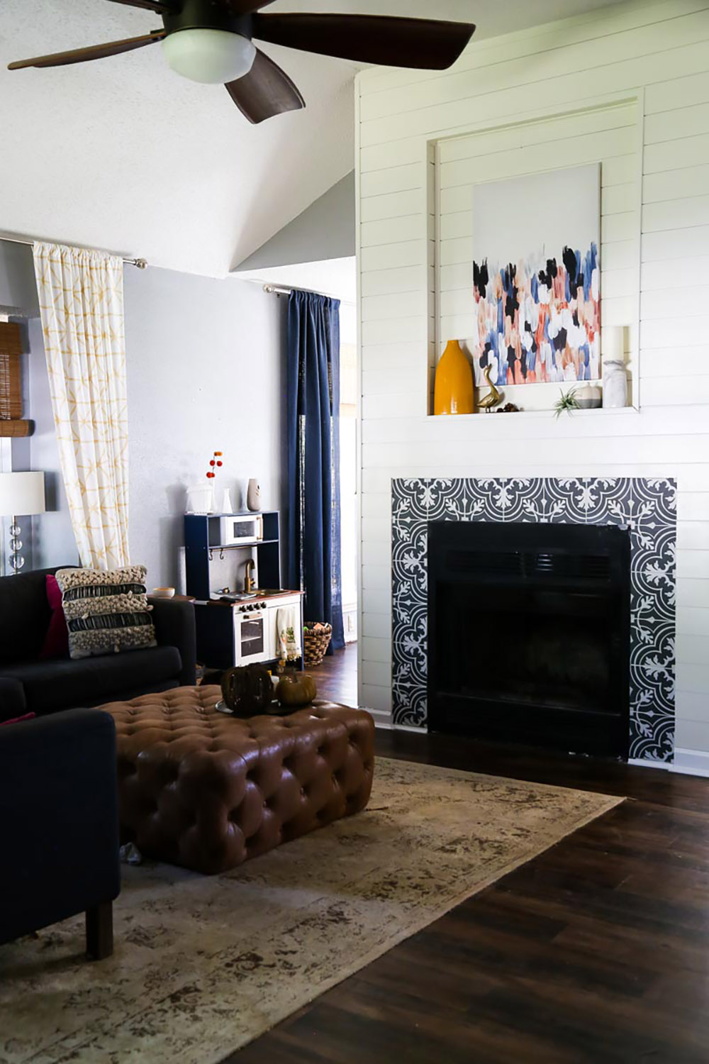 A living room with furniture and a fireplace with mosaic tile, shiplap and wall art.