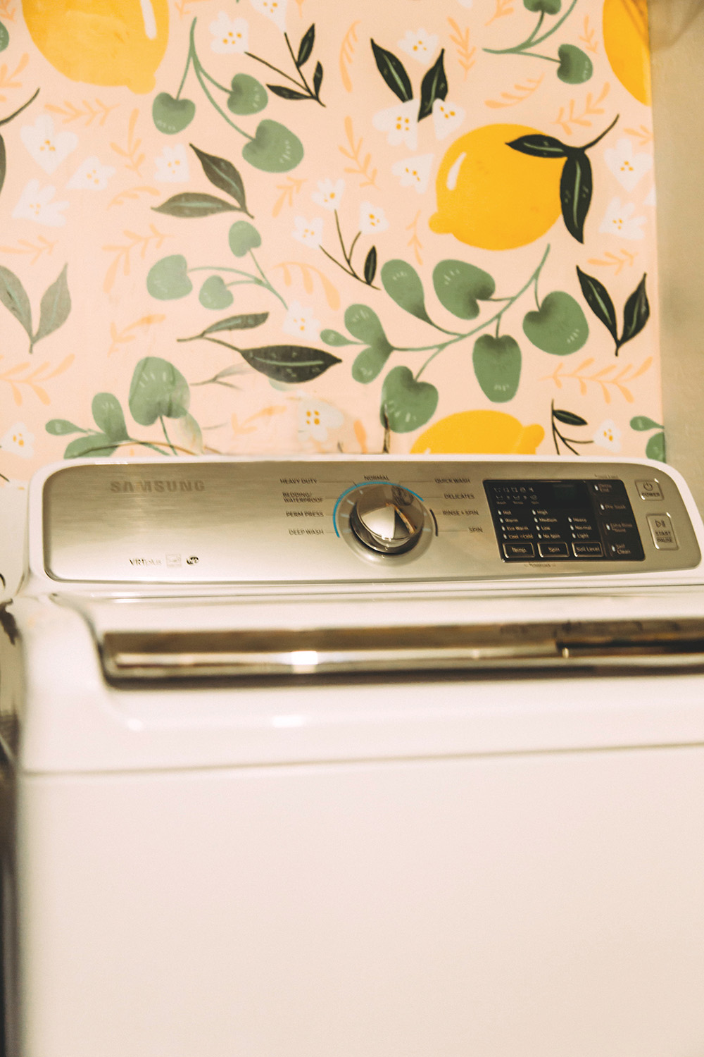A white Samsung top-load washer in front of a colorful wall with lemons.
