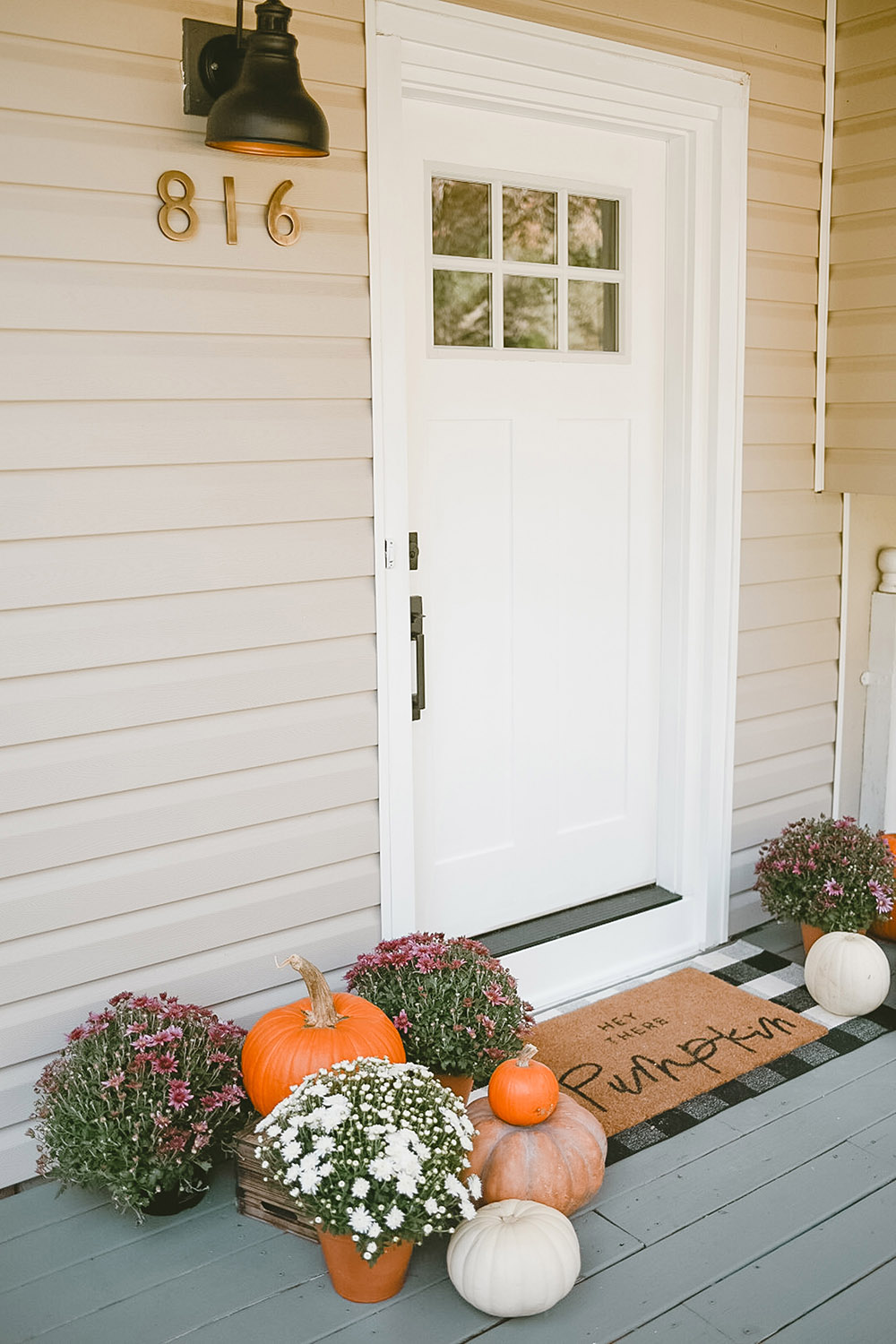 A new white front door with hardware is surrounded by pumpkins and mums.