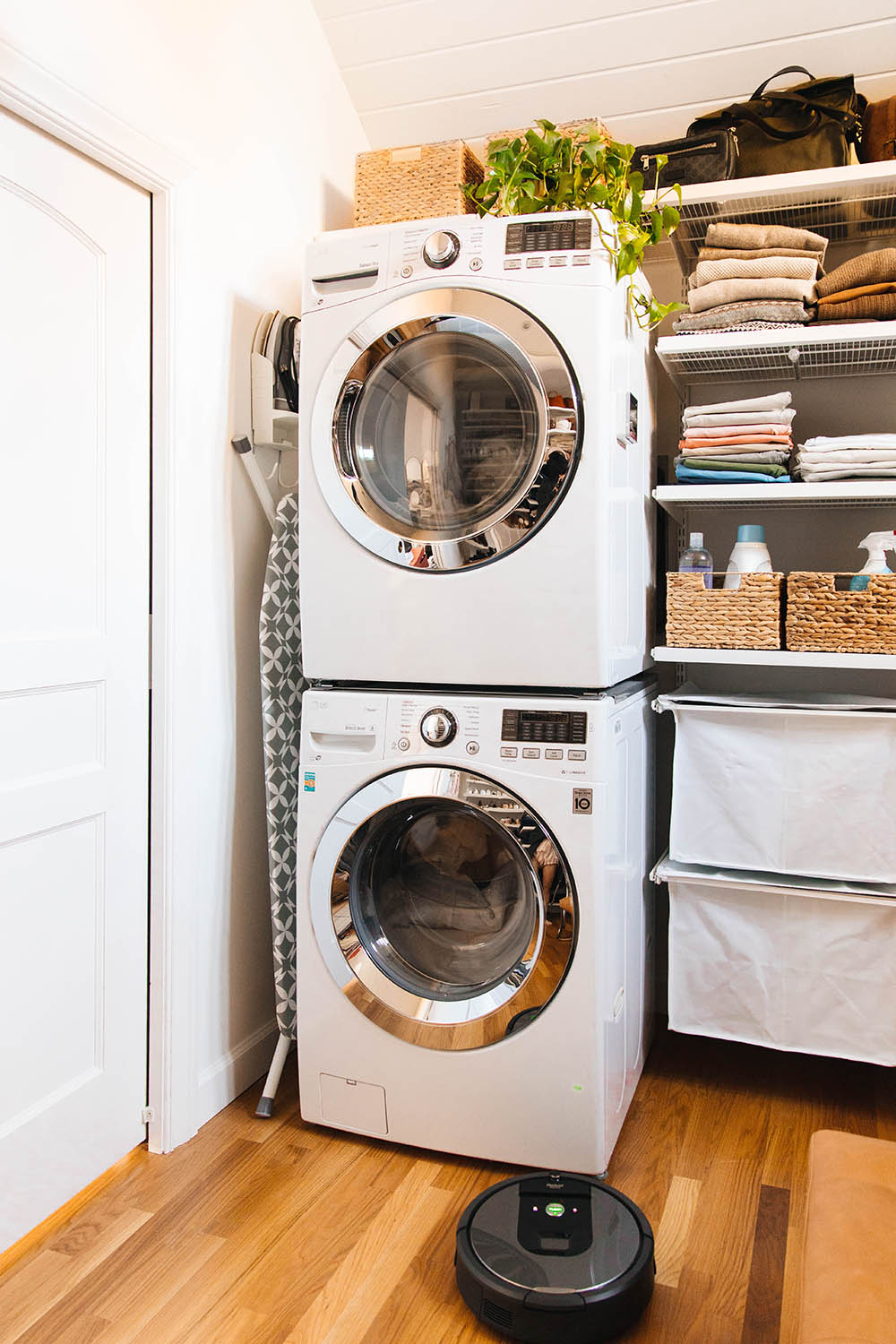 A laundry room with white LG front load laundry appliances, shelving, and a Roomba.