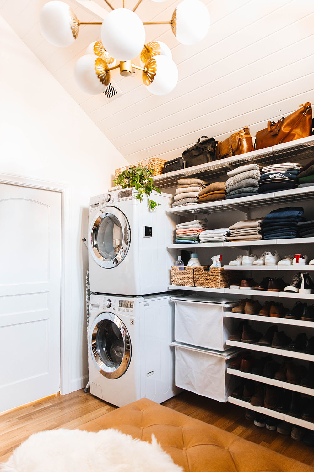 A laundry room with a pair of stacked LG laundry appliances, a hanging chandelier, and a wall of open storage.