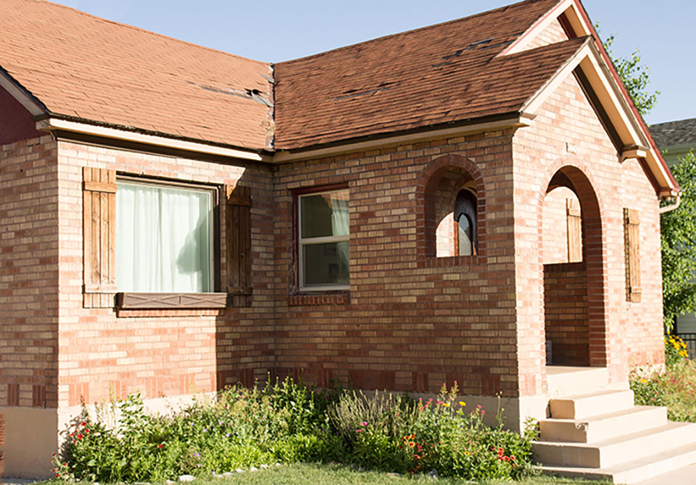 A brick home with an old roof and yard that has not been landscaped.