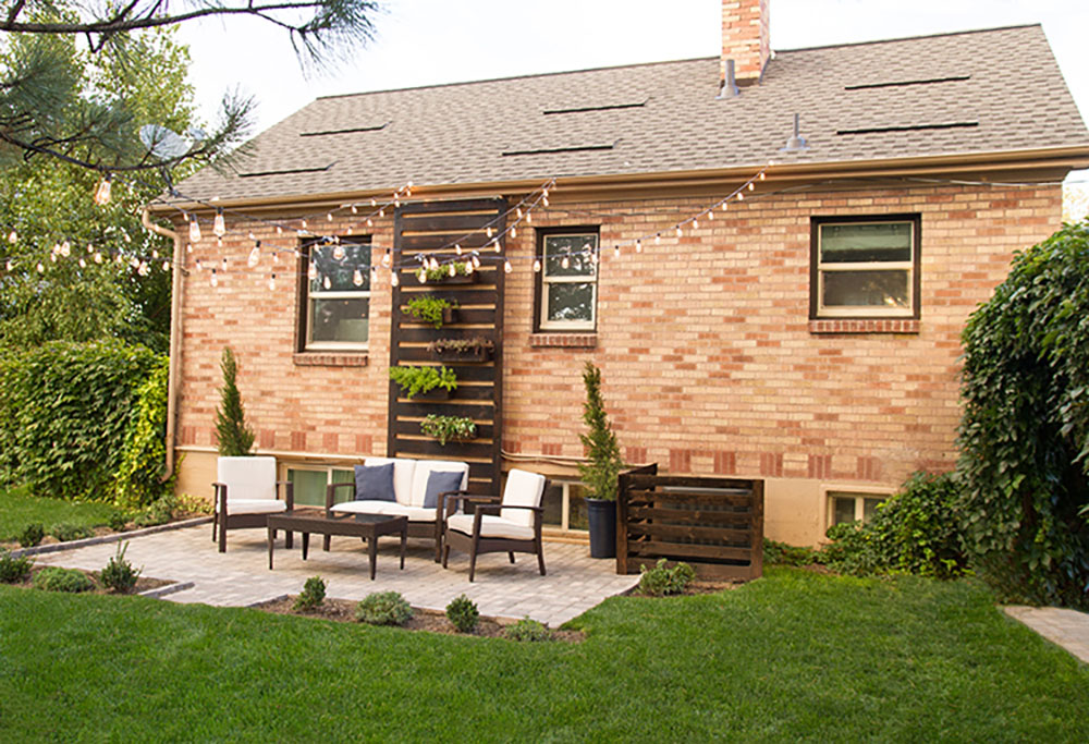 The backyard of a brick home decorated with dark wood patio furniture.