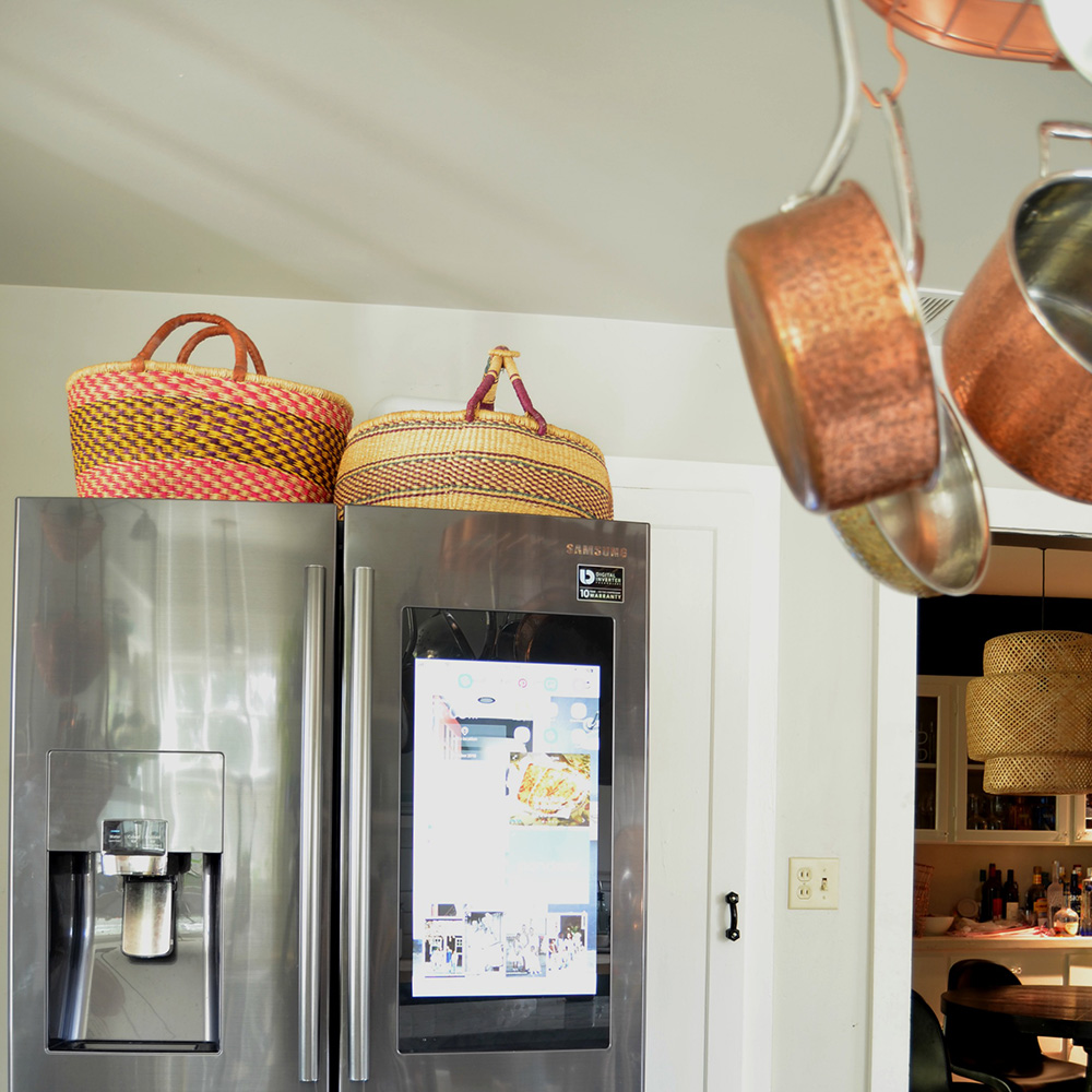 A group of copper pots hangs in front of a smart refrigerator.