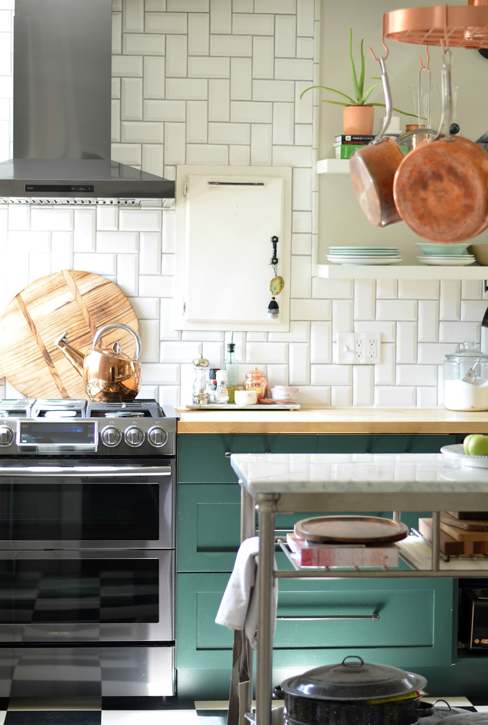 A kitchen with teal lower cabinets, butcher block countertops, and a white tile backsplash.