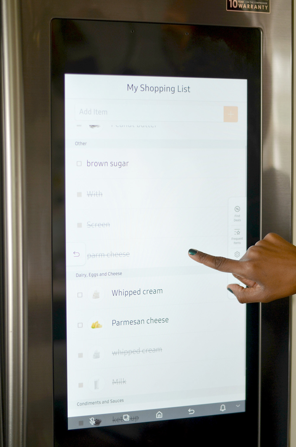 A person creates a shopping list on the screen of a smart refrigerator.