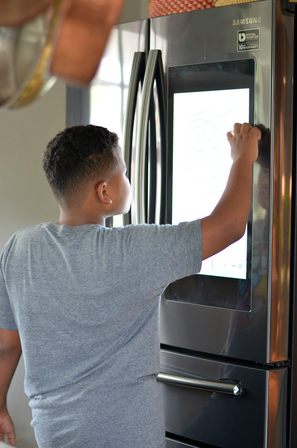 A young boy touches the screen display on a Samsung smart refrigerator.