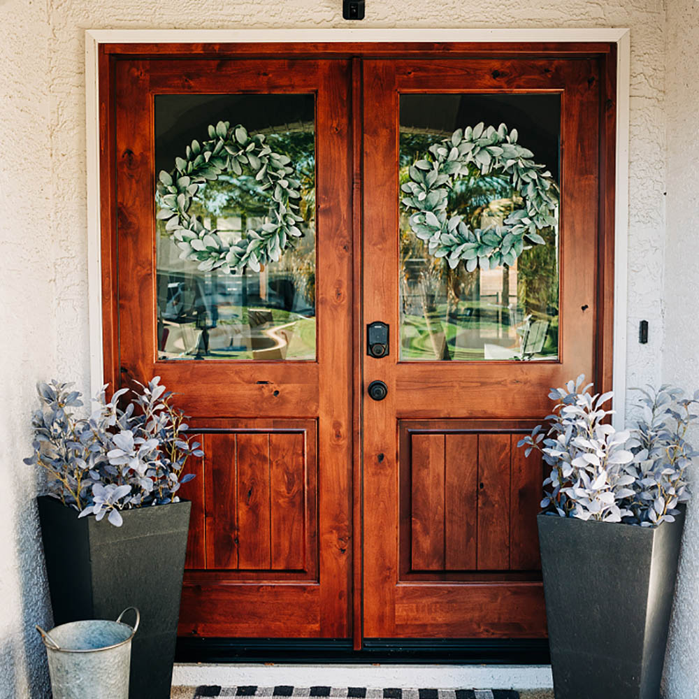 A front entryway with double wooden front doors decorated with greenery.