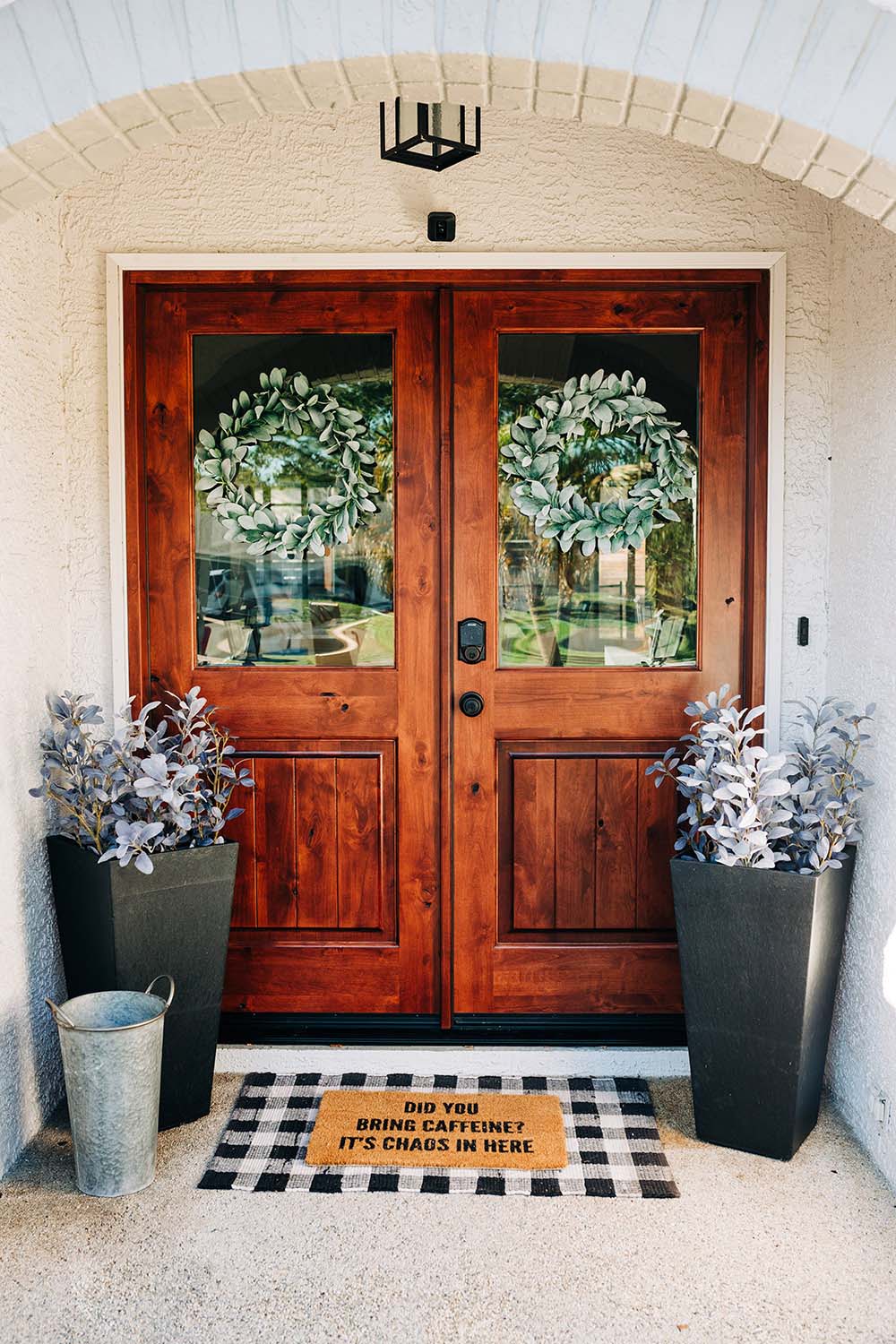 A modern entryway with layered doormats and large black planters.