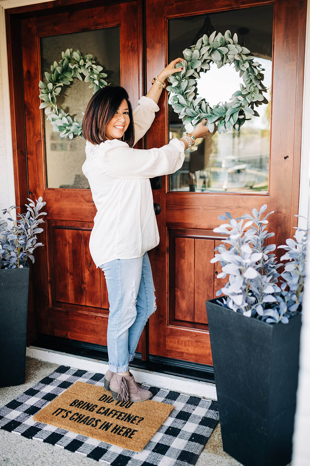 A woman adjusting a faux green wreath on a front door.