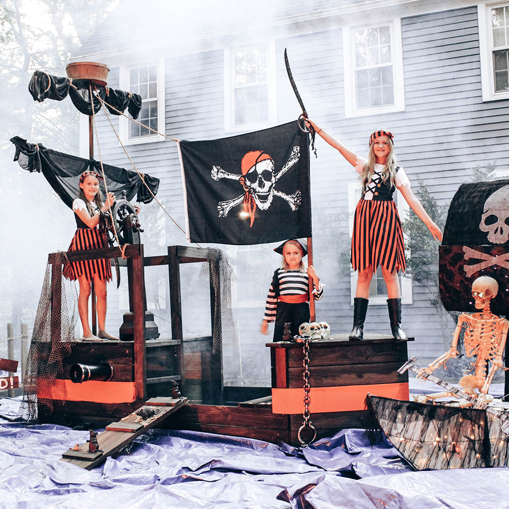 Three children dressed as pirates stand on a pirate ship.