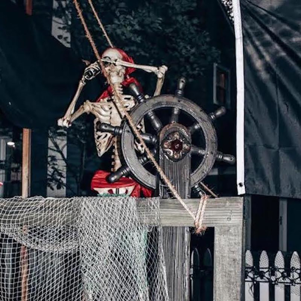 A skeleton pirate looking through a telescope next to the wheel of a pirate ship.