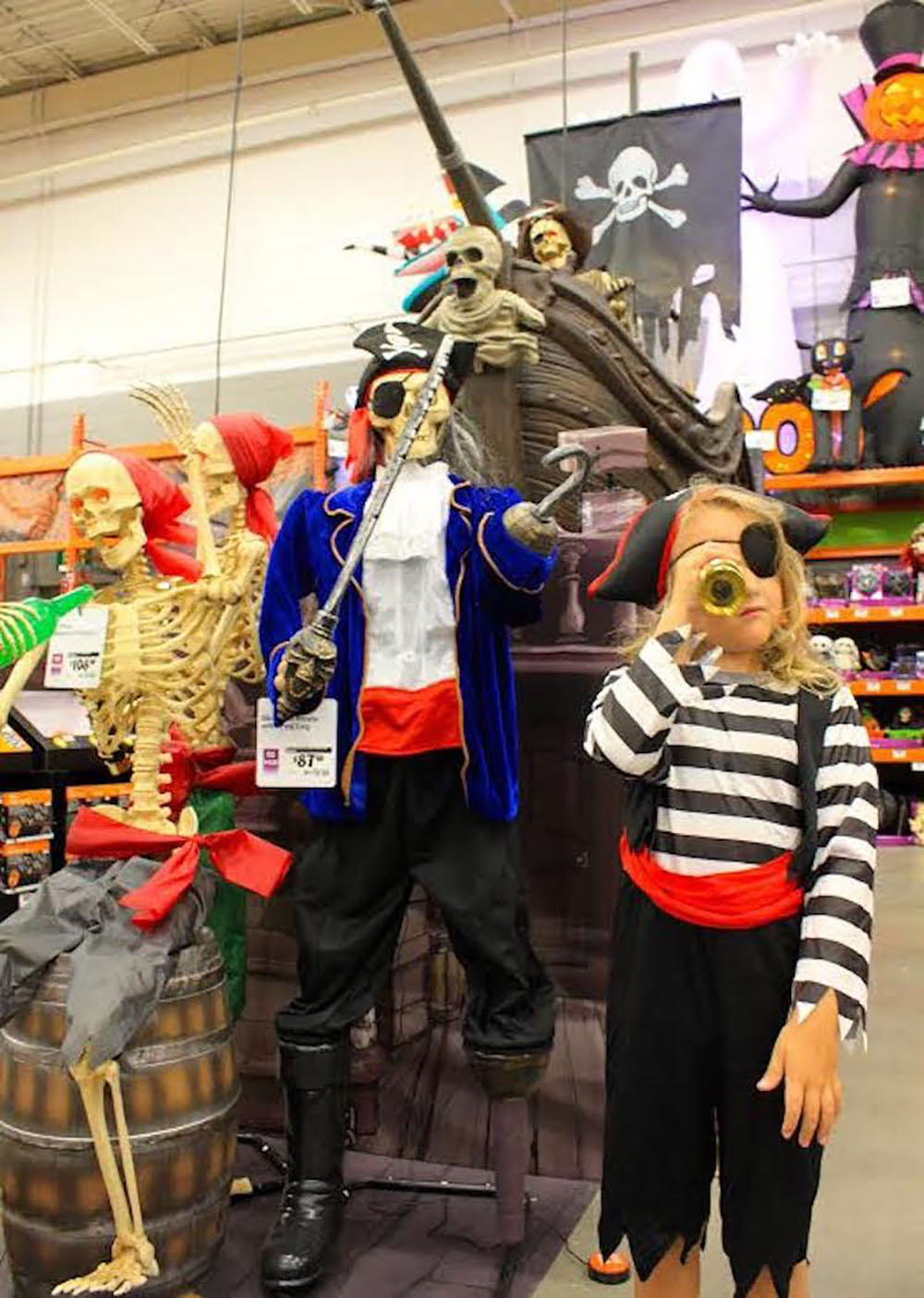 A child dressed as a pirate stands next to a skeleton pirate inside The Home Depot.
