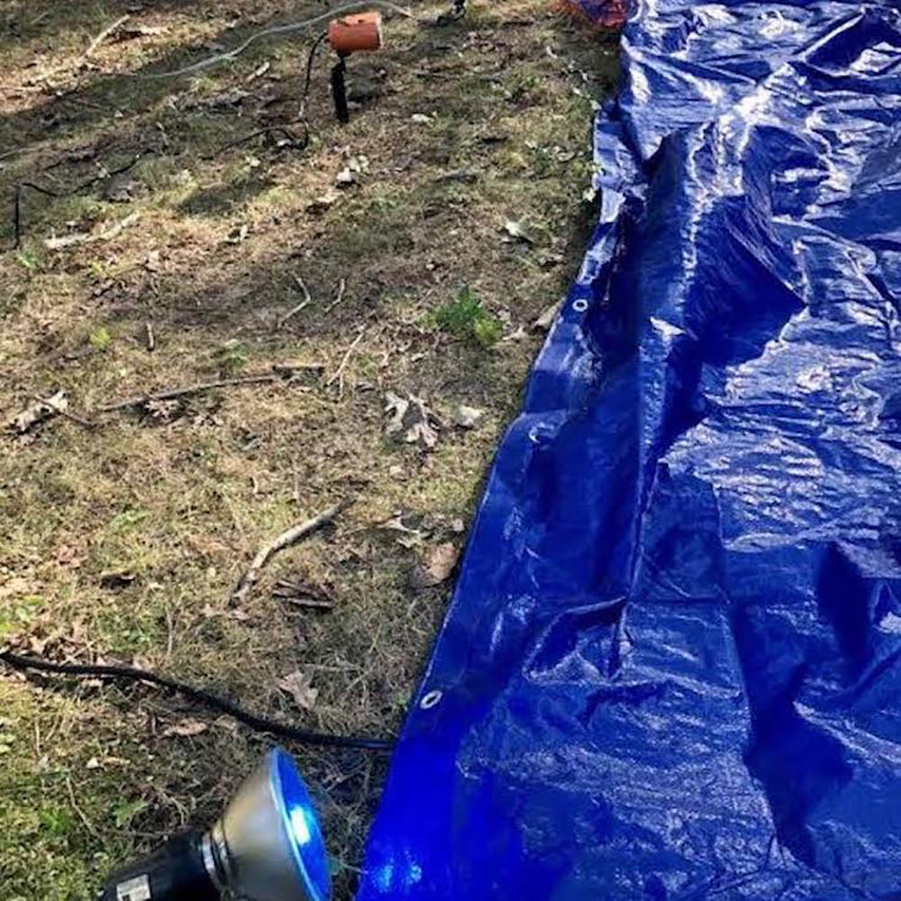 A blue tarp over grass next to spotlights.