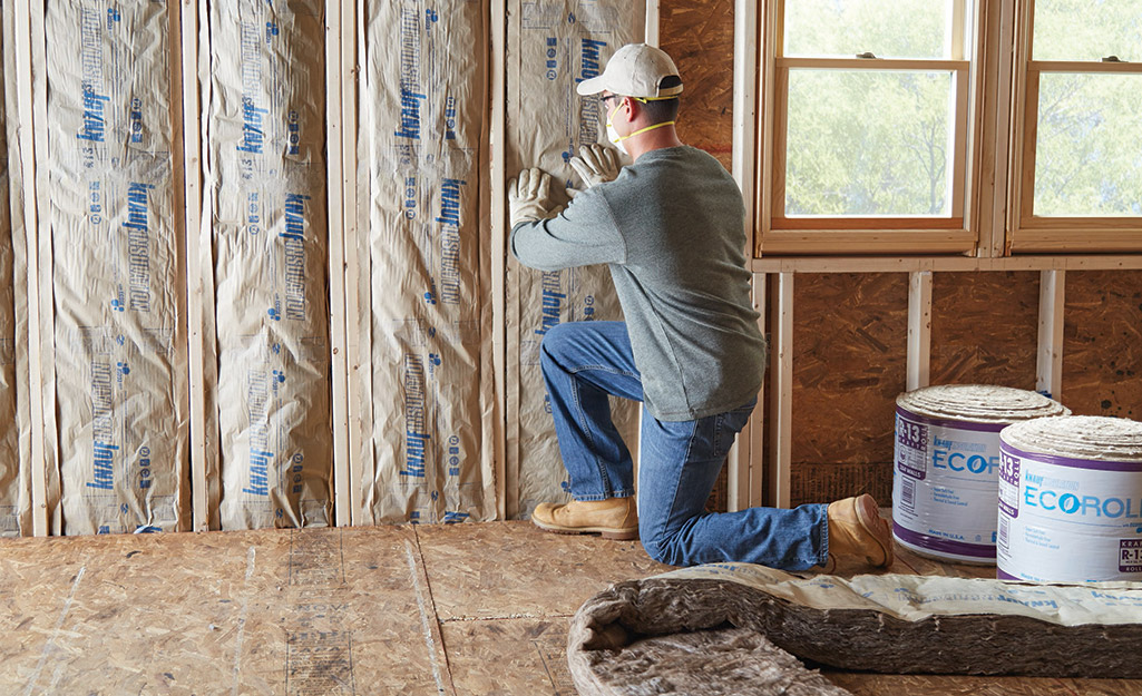 A person installing insulation batts in unfinished exterior walls.