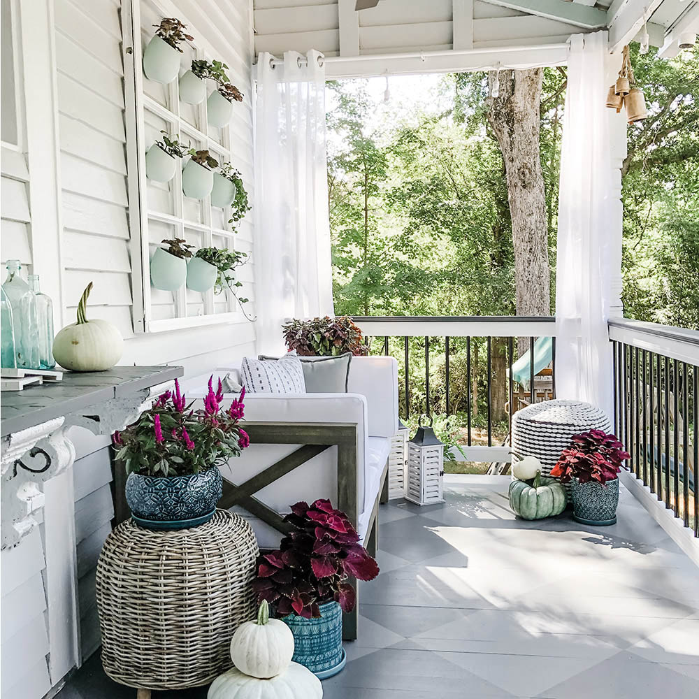 A porch decorated with planters, pumpkins, and outdoor seating.