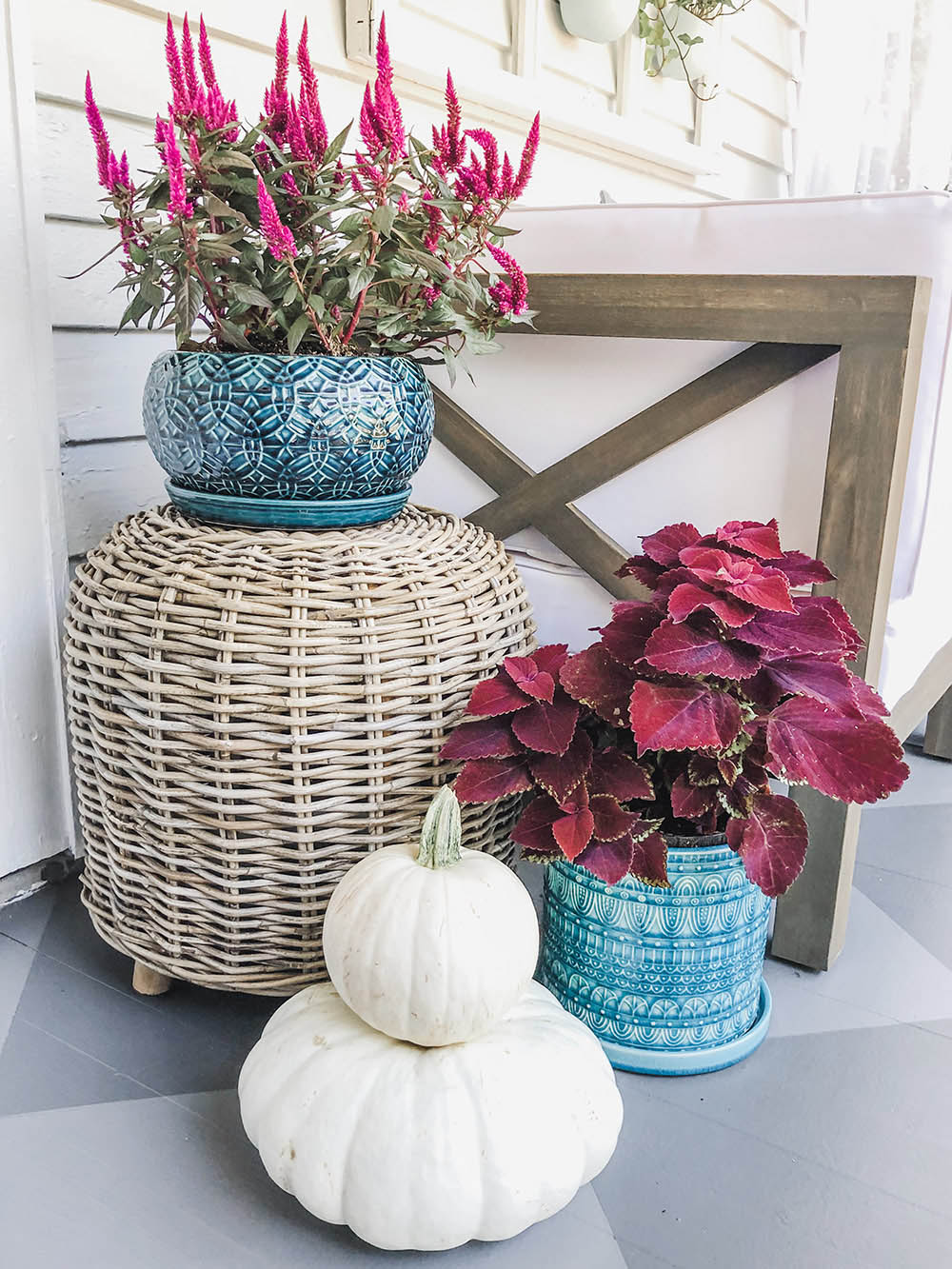 Two blue planters with pink plants next to white stacked pumpkins.