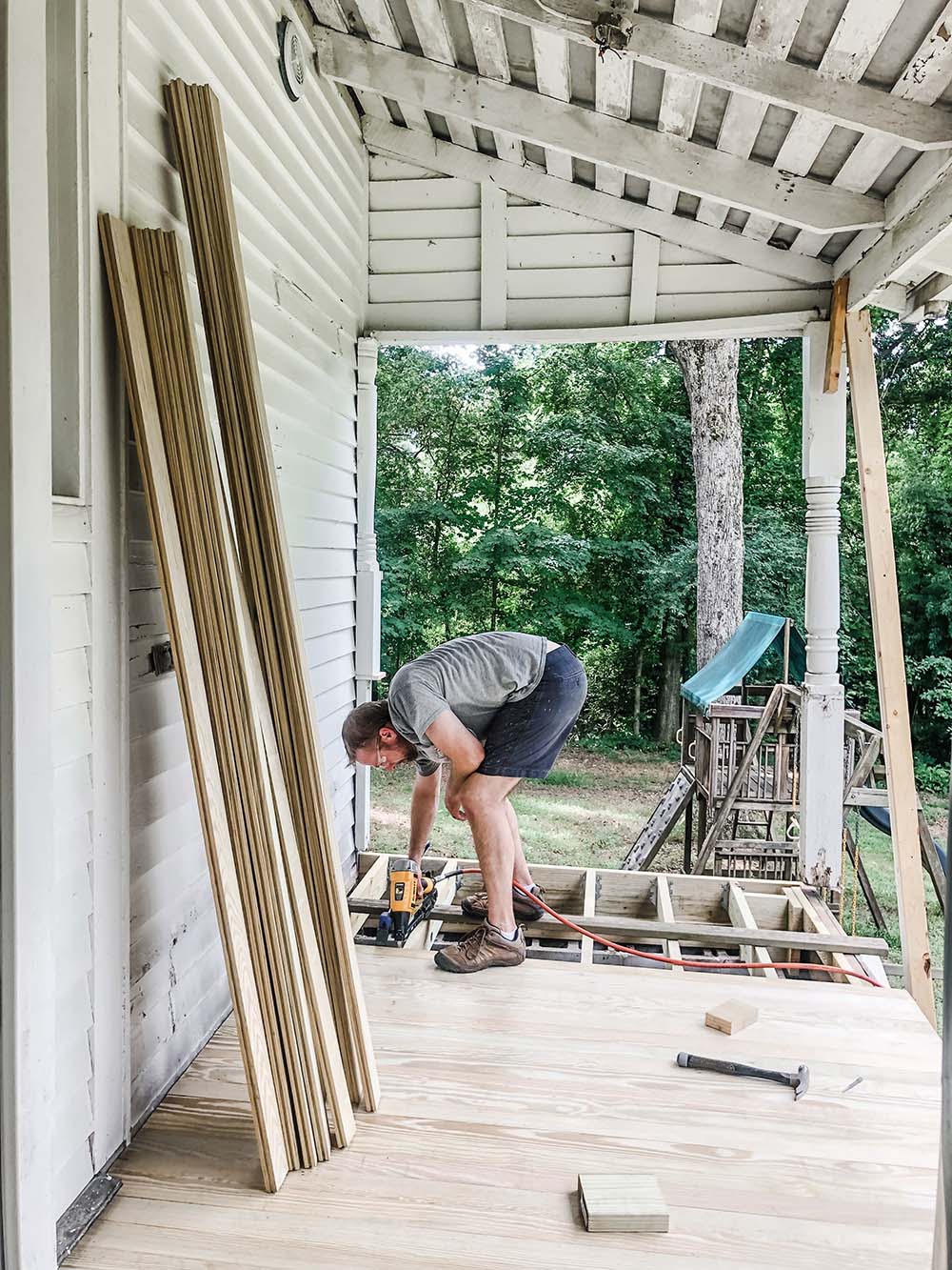 A man installs new wood flooring to a porch floor.