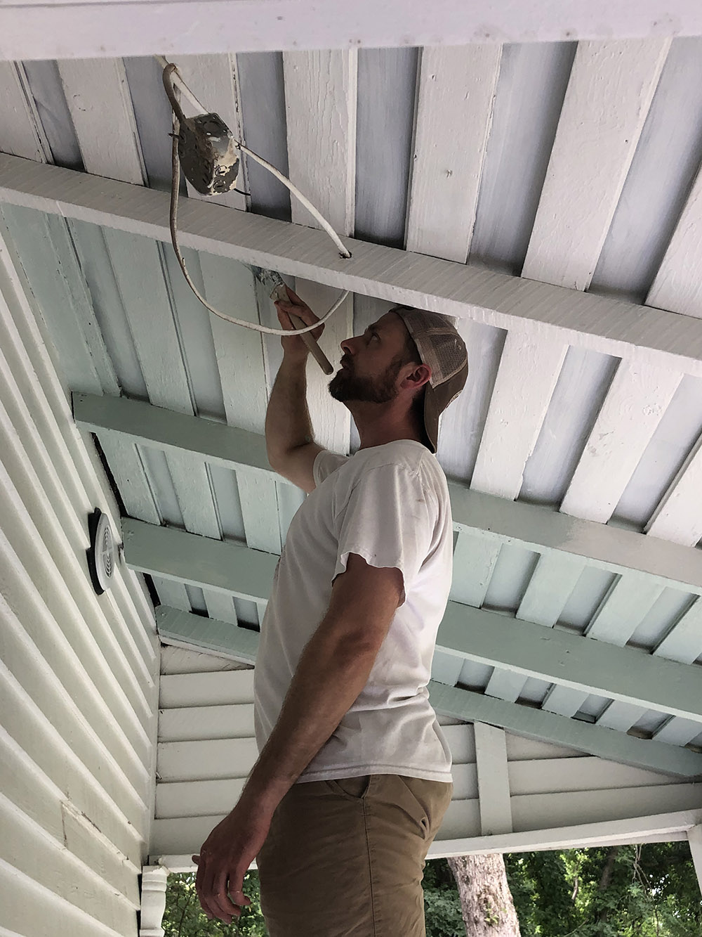 A man paints the ceiling of a porch in a light blue color.