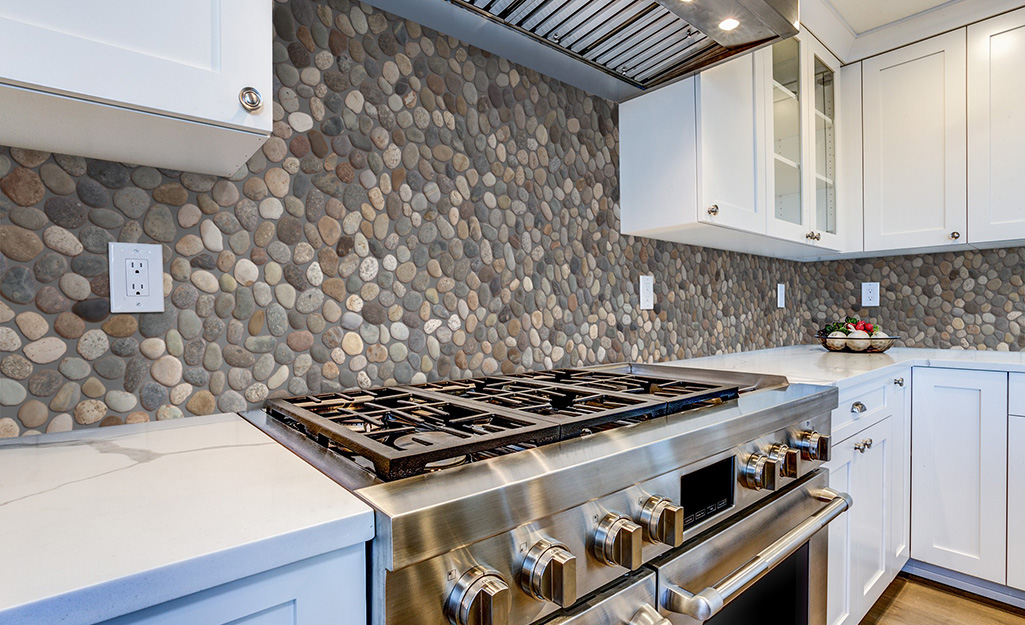 A stone backsplash gives an earthy feel to a kitchen with white cabinets and stainless steel.