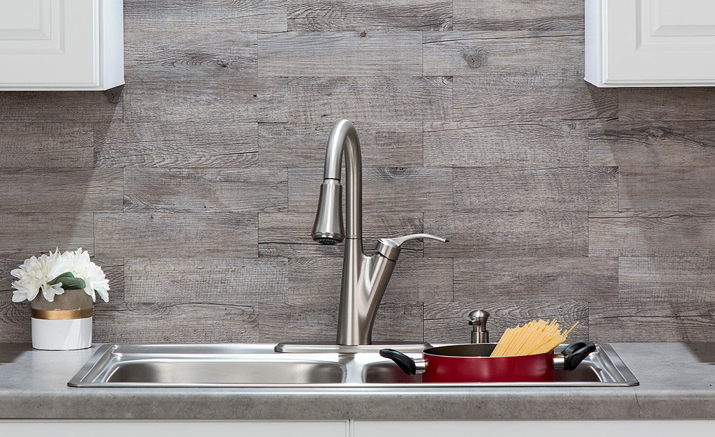 A gray wood backsplash behind a sink gives a rustic and natural vibe.