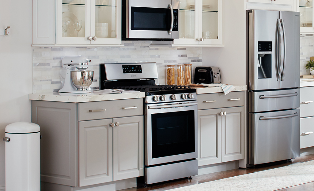 Monochromatic white and gray tiles are a matching backsplash for a large kitchen with stainless steel appliances.