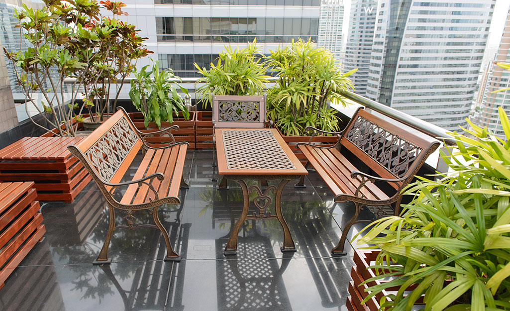 Benches and table surrounded by greenery on an apartment balcony.