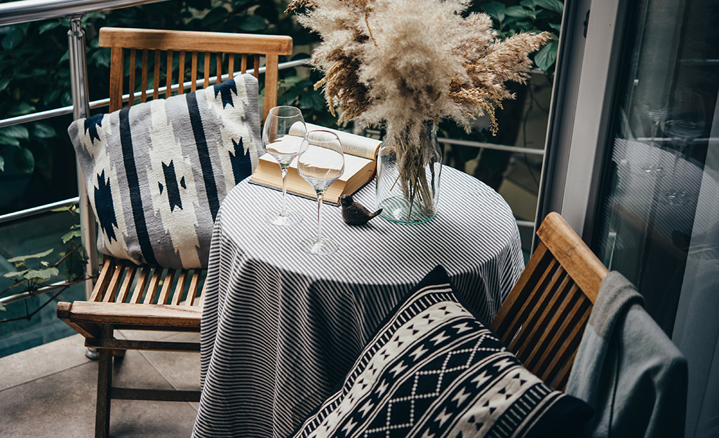 Round table covered in gray print tablecloth with complementary pillows on balcony.