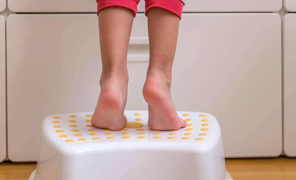 Child using a step stool at a bathroom sink.