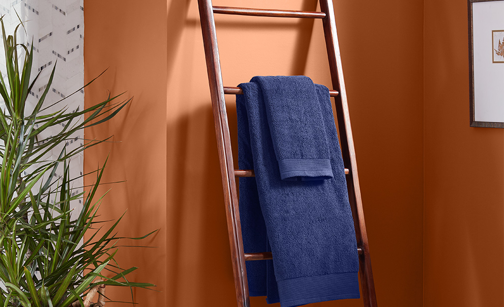 Leaning storage ladder with a blue towel on it, leaning against an orange wall.