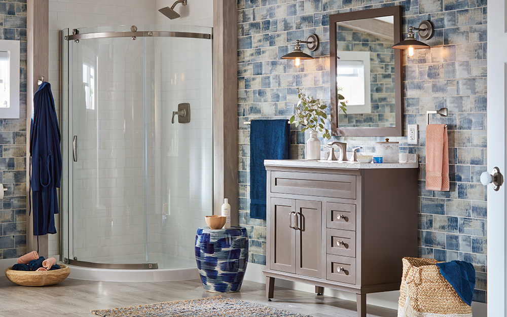 A bathroom features a blue and gray patterned wall tile, gray vanity and a walk-in shower with a curved glass door