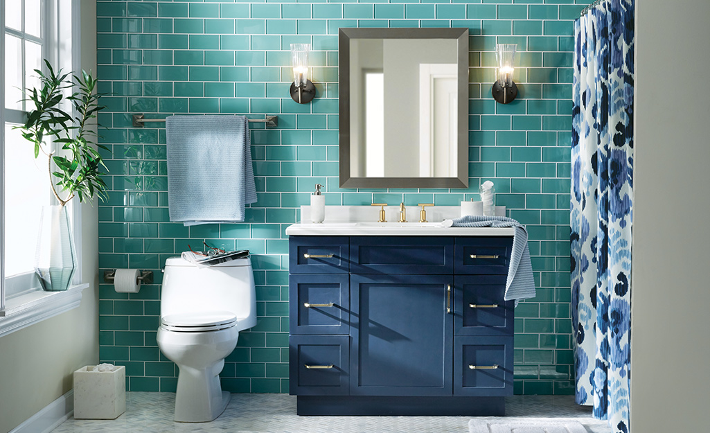 Green subway wall tile in a bathroom with a blue vanity and gray patterned floor tiles.