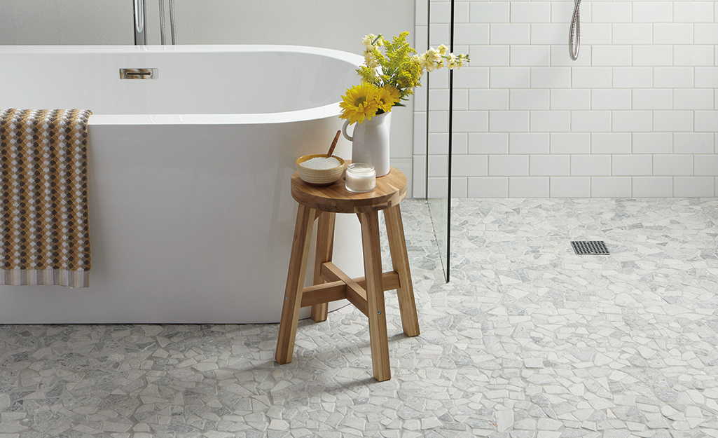 Stone-patterned tile in a bathroom with a tub and wooden stool.