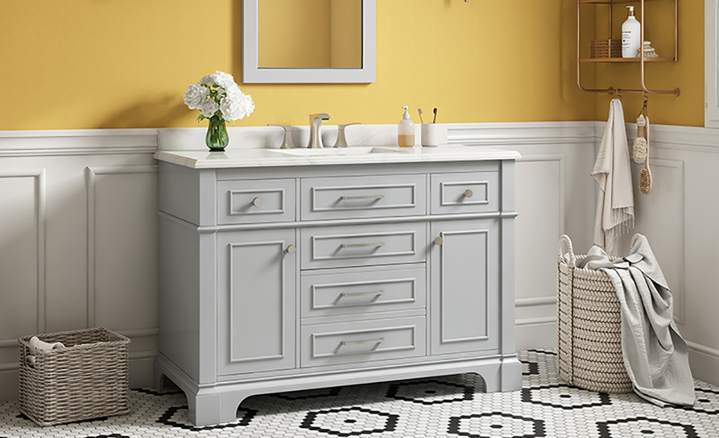 A gray bathroom vanity in a yellow bathroom with white wainscoting.