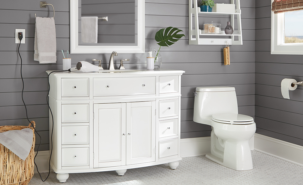 A white furniture-style coastal vanity in a gray wood-paneled bathroom.