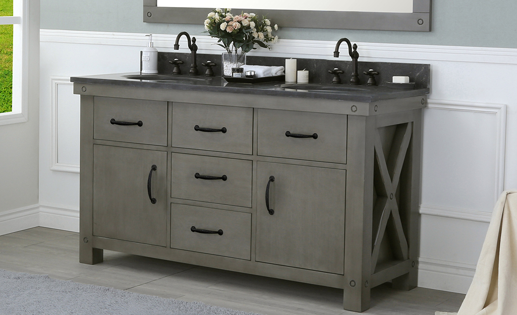 A distressed gray industrial bathroom vanity with rustic detailing and a dark countertop.