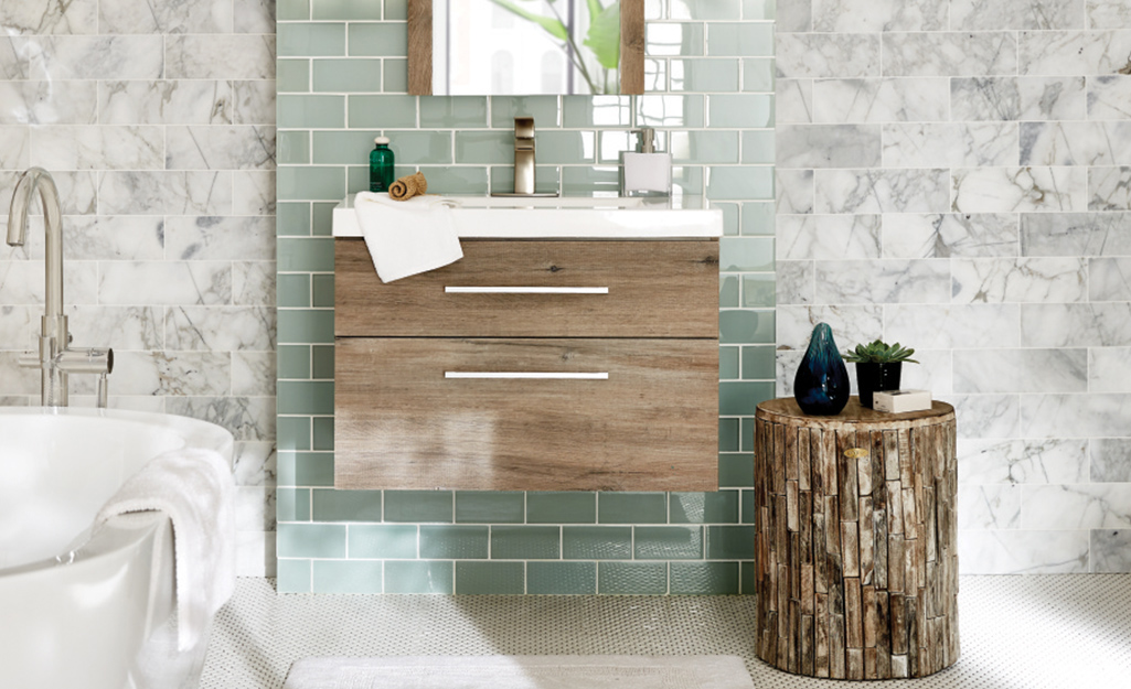 Light wood floating vanity mounted to a green tile wall.