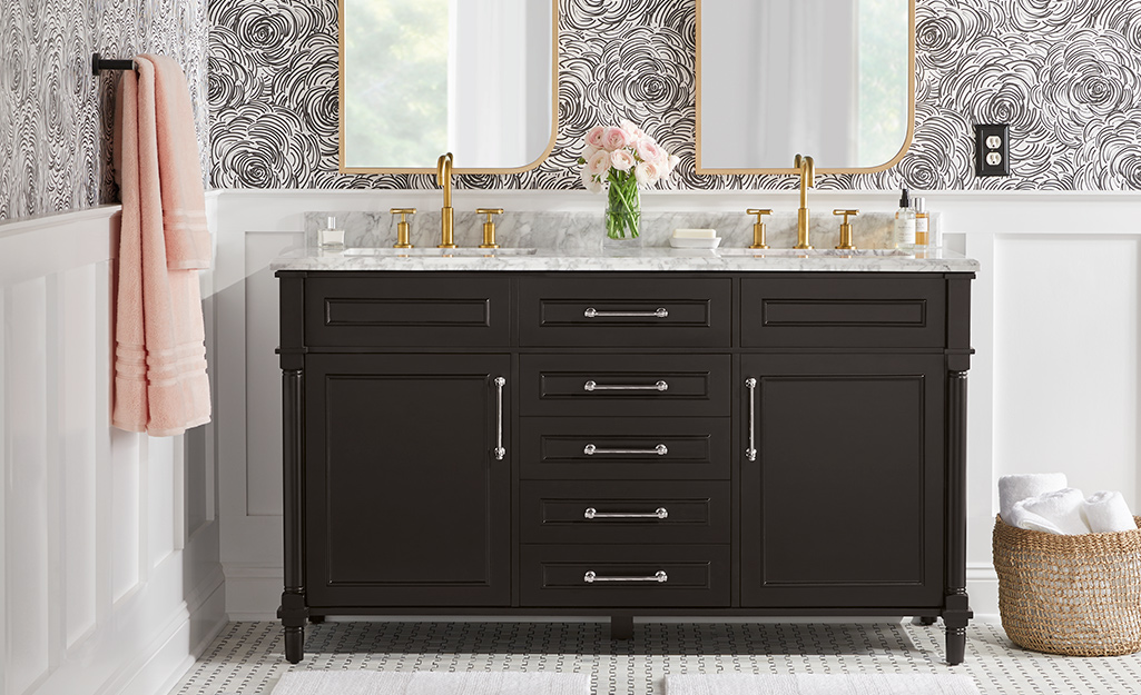 A black bathroom vanity with silver pulls and gold faucets.