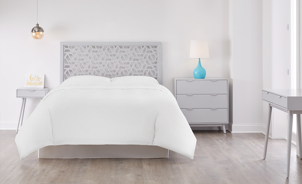 An all-white bedroom wall with grey furniture.