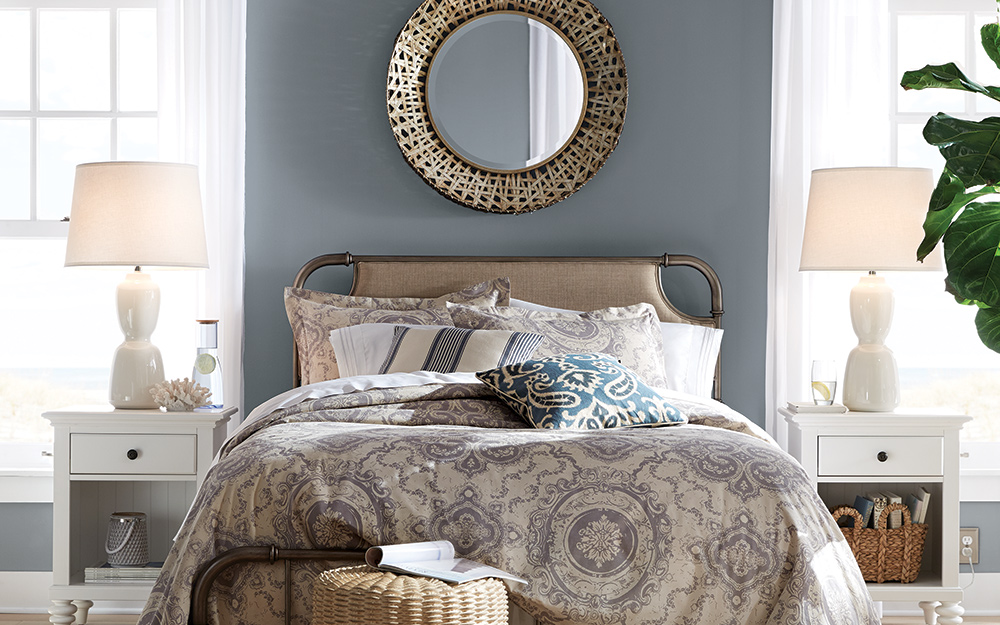 Bedroom with grey walls, a bed, nightstand and hanging mirror.