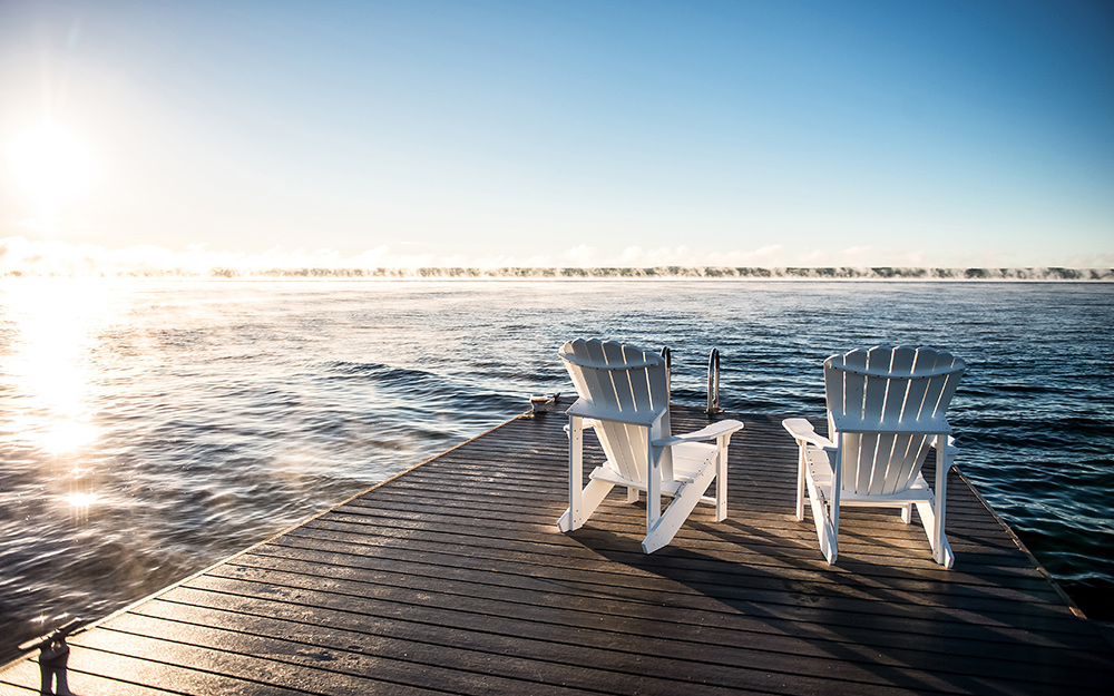 Two chairs on a wooden dock at a lake.