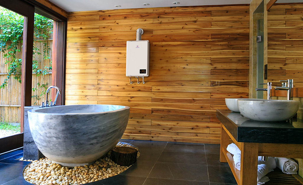 A tankless water heater hangs on the wood-paneled wall of a bathroom with bowl sinks and a circular bathtub.