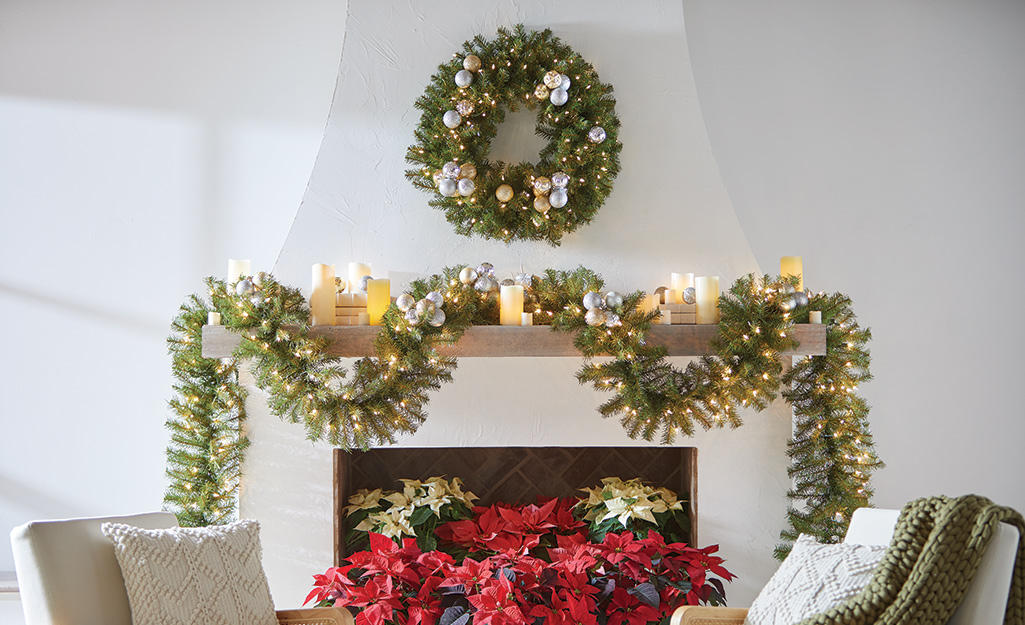 A garland and wreath with greenery and flowers enlivens a fireplace mantle.