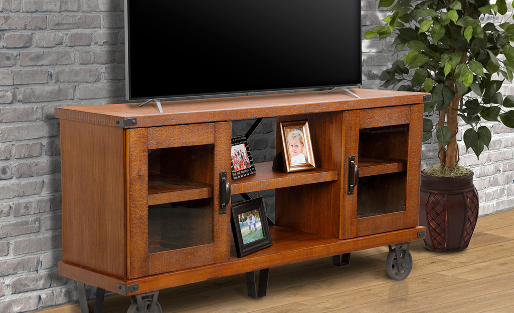 A picture of a flat-screen TV stand built of wood with steel caster wheels.